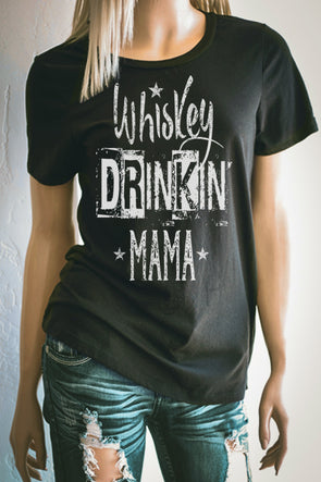 Pictured is a woman wearing a black T Shirt. The graphic is made up of different distressed typefaces that say Whiskey Drinkin' Mama. Very cute t shirt for casual times on the weekend!