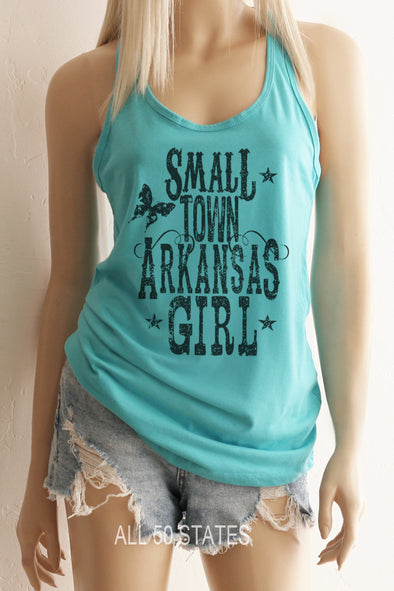 Pictured is a girl with a Cancun Blue Racerback Tank Top with a graphic that is distressed looking with vintage looking western type that says "Small Town Arkansas Girl with some stars and a graphic Butterfly and swirls.