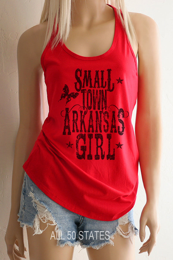 Pictured is a girl with a Red Racerback Tank Top with a graphic that is distressed looking with vintage looking western type that says "Small Town Arkansas Girl with some stars and a graphic Butterfly and swirls.