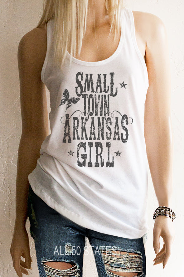 Pictured is a girl with a White Racerback Tank Top with a graphic that is distressed looking with vintage looking western type that says "Small Town Arkansas Girl with some stars and a graphic Butterfly and swirls.